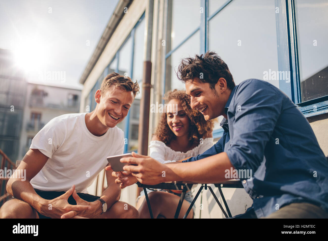 Tre giovani amici seduti all'aperto e guardando il telefono cellulare. Gruppo di persone sedute al cafe esterno e guardare i video su Foto Stock