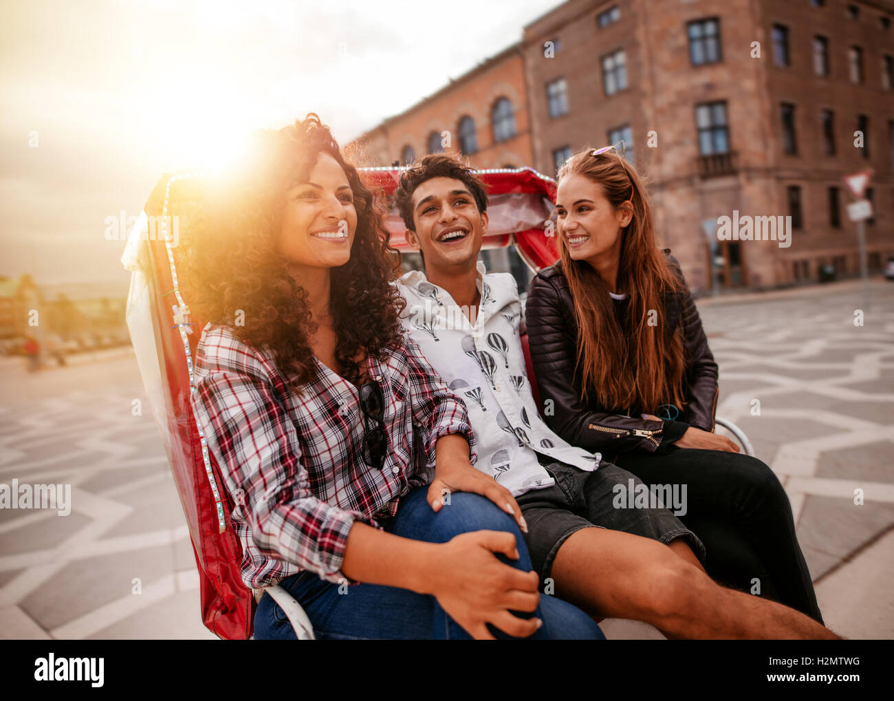 Tre giovani divertirsi sul triciclo nella città. Giovani uomini e donne equitazione su triciclo sulla strada e sorridente. Foto Stock