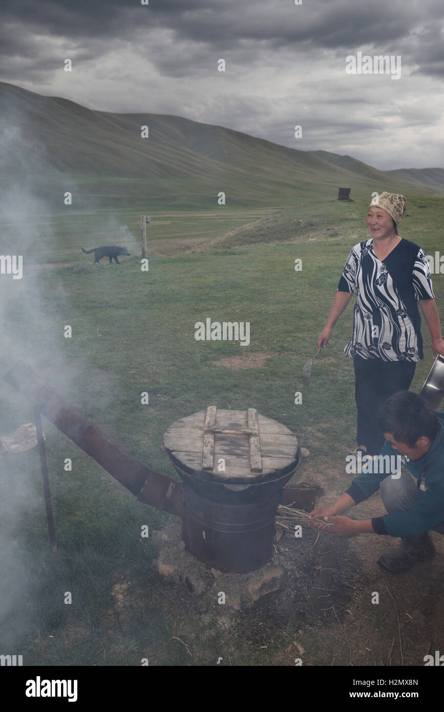 Figlio addensarsi di fuoco sul forno esterno cottura agnello con madre ridere sul Plateau Assy Kazakistan Foto Stock