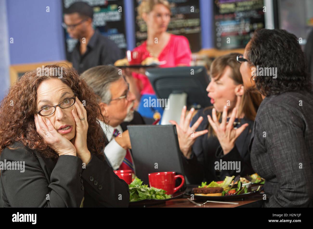 Annoiato donna con Co-Workers in Cafe Foto Stock