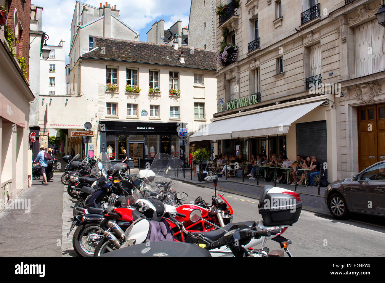 Le persone hanno il pranzo in uno dei ristoranti nel quartiere di Le Marais di Parigi. Molte moto parcheggiate su strada. Foto Stock