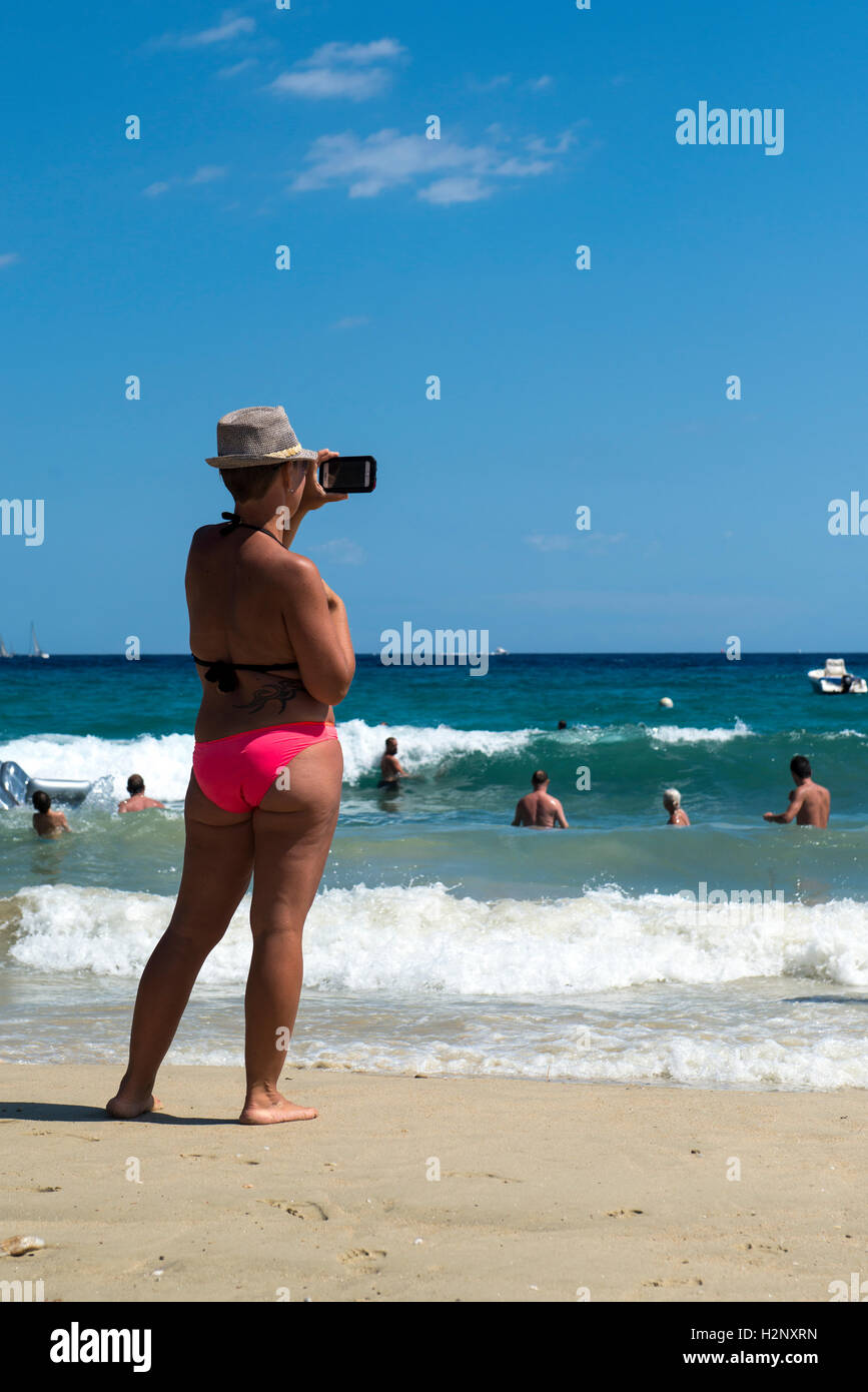 Donna di scattare una foto con uno smartphone sulla spiaggia di Le Lavandou, Regione Provenza-Alpi-Costa Azzurra, Francia Foto Stock