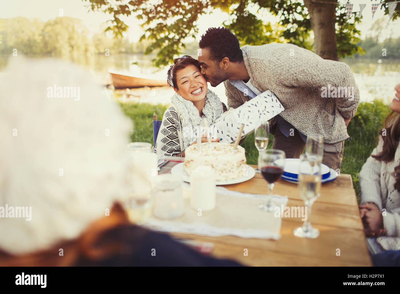 Fidanzato baciare fidanzata con il regalo di compleanno a Lakeside patio tabella Foto Stock