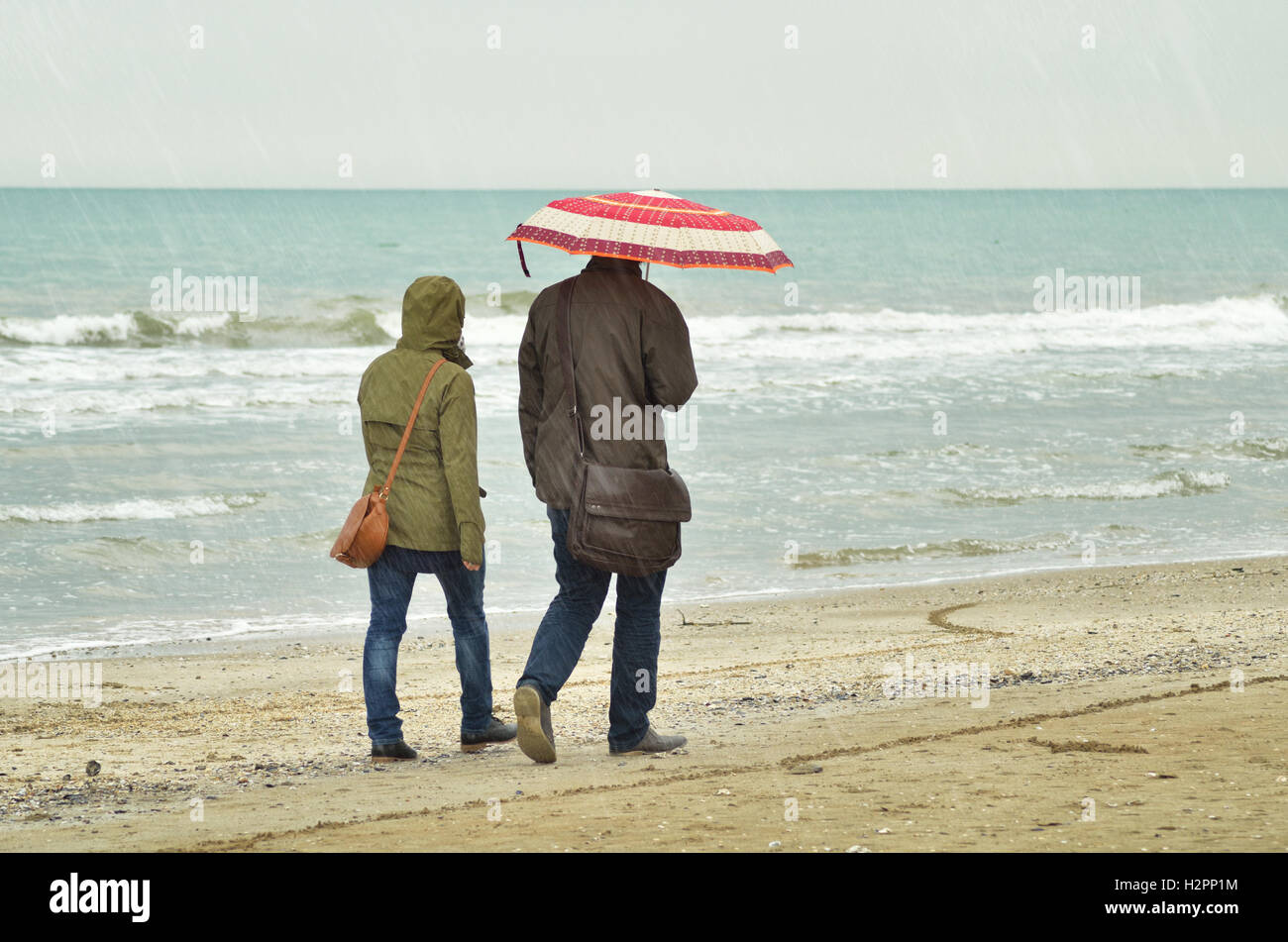 Coppia con ombrello sotto la pioggia sul litorale Foto Stock