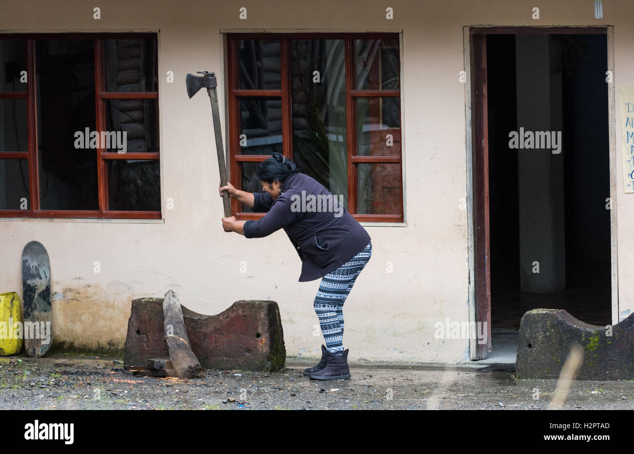 Una donna locale di legna da ardere di trinciatura con un'ascia di fronte alla sua casa. Ecuador, Sud America. Foto Stock