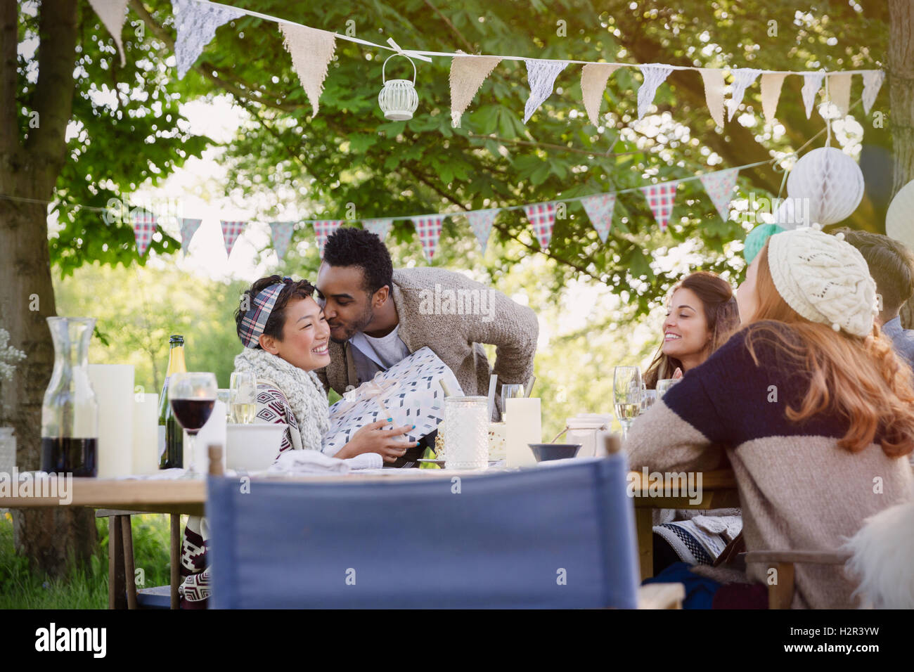 Fidanzato baciare fidanzata con il regalo di compleanno a party in giardino tavolo Foto Stock