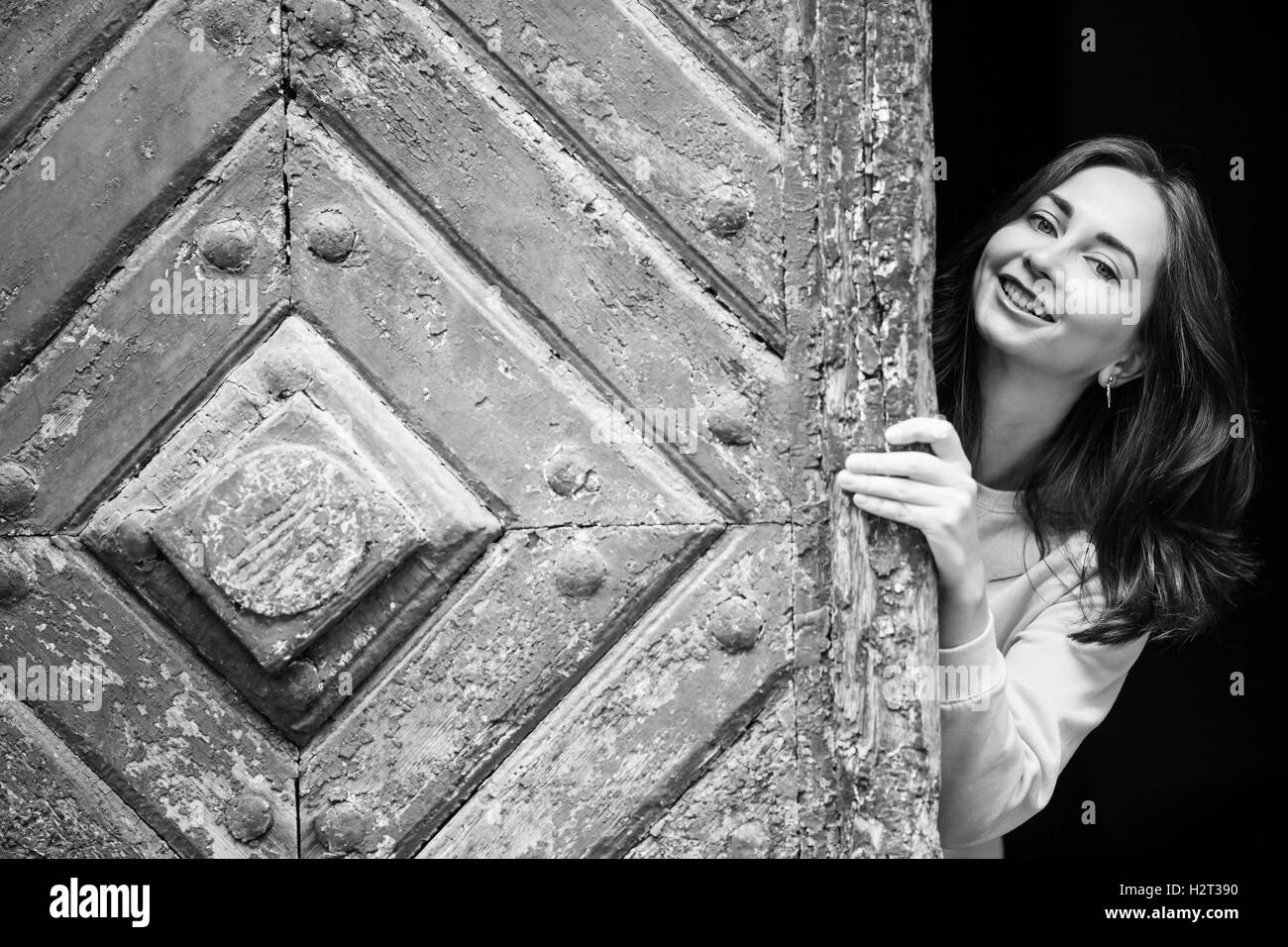 Ragazza giovane e carina del peering da dietro l antica porta di legno, in bianco e nero photo. Foto Stock