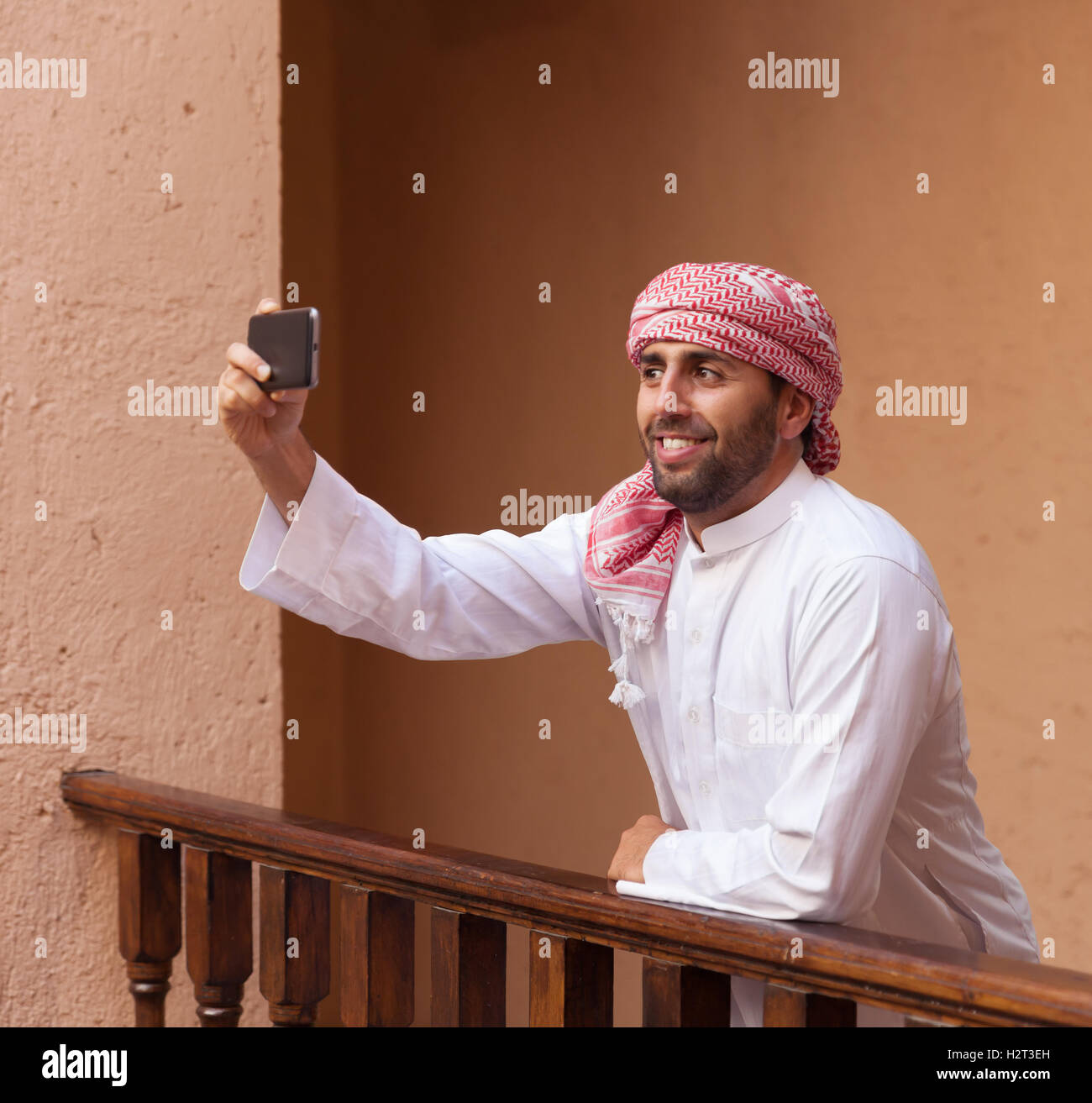 Giovani sorridente bello uomo arabo in abiti tradizionali prende smartphone selfie Foto Stock