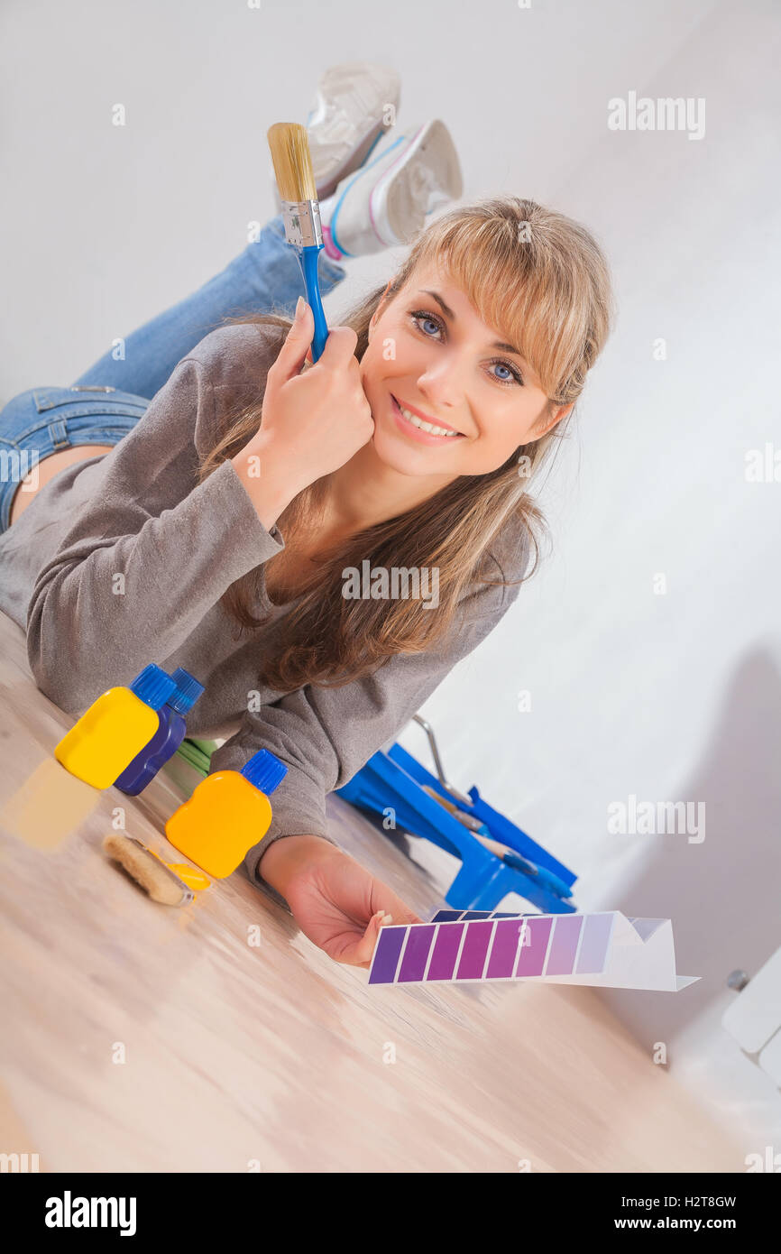 Bella donna sorridente giace sul pavimento in legno tenendo il pennello Foto Stock