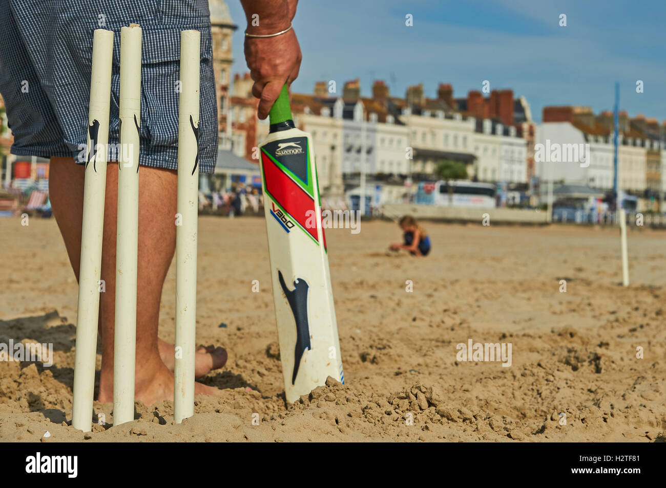 Famiglia e amici che si godono una partita di cricket spiaggia su una spiaggia di sabbia. Foto Stock