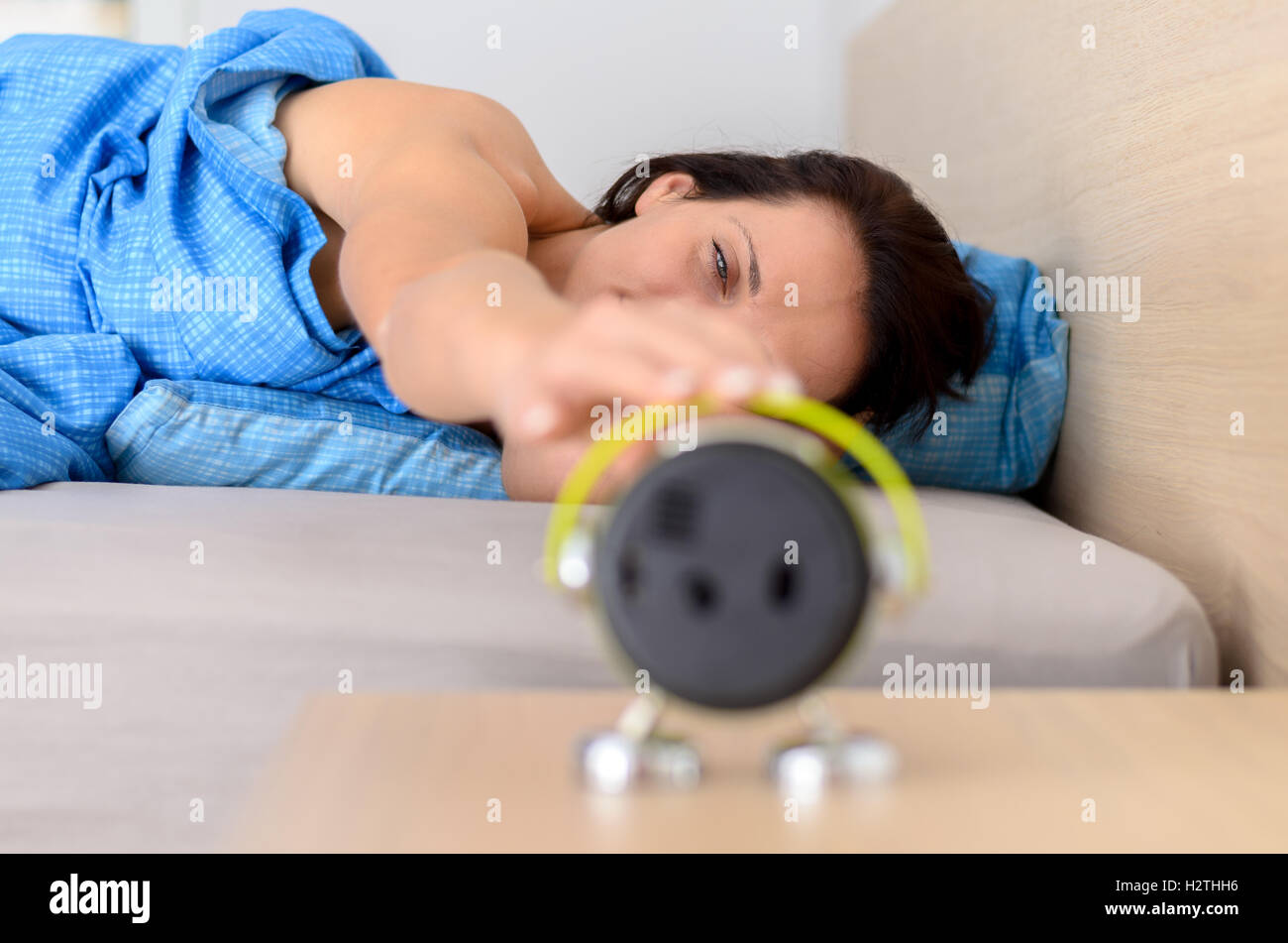 La donna che si allunga per spegnere la sveglia come si risveglia la sua al mattino, vicino della messa a fuoco per gli occhi Foto Stock