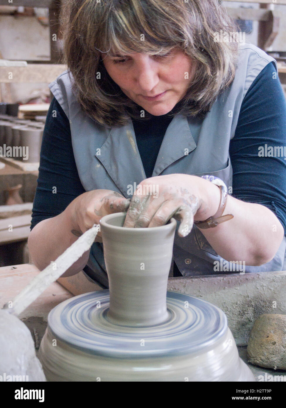 Gettare una pentola su una ruota in ceramica. Un craftswoman solleva i bordi di un bicchiere su una ruota che gira. Le sue mani sono coperti di fango Foto Stock