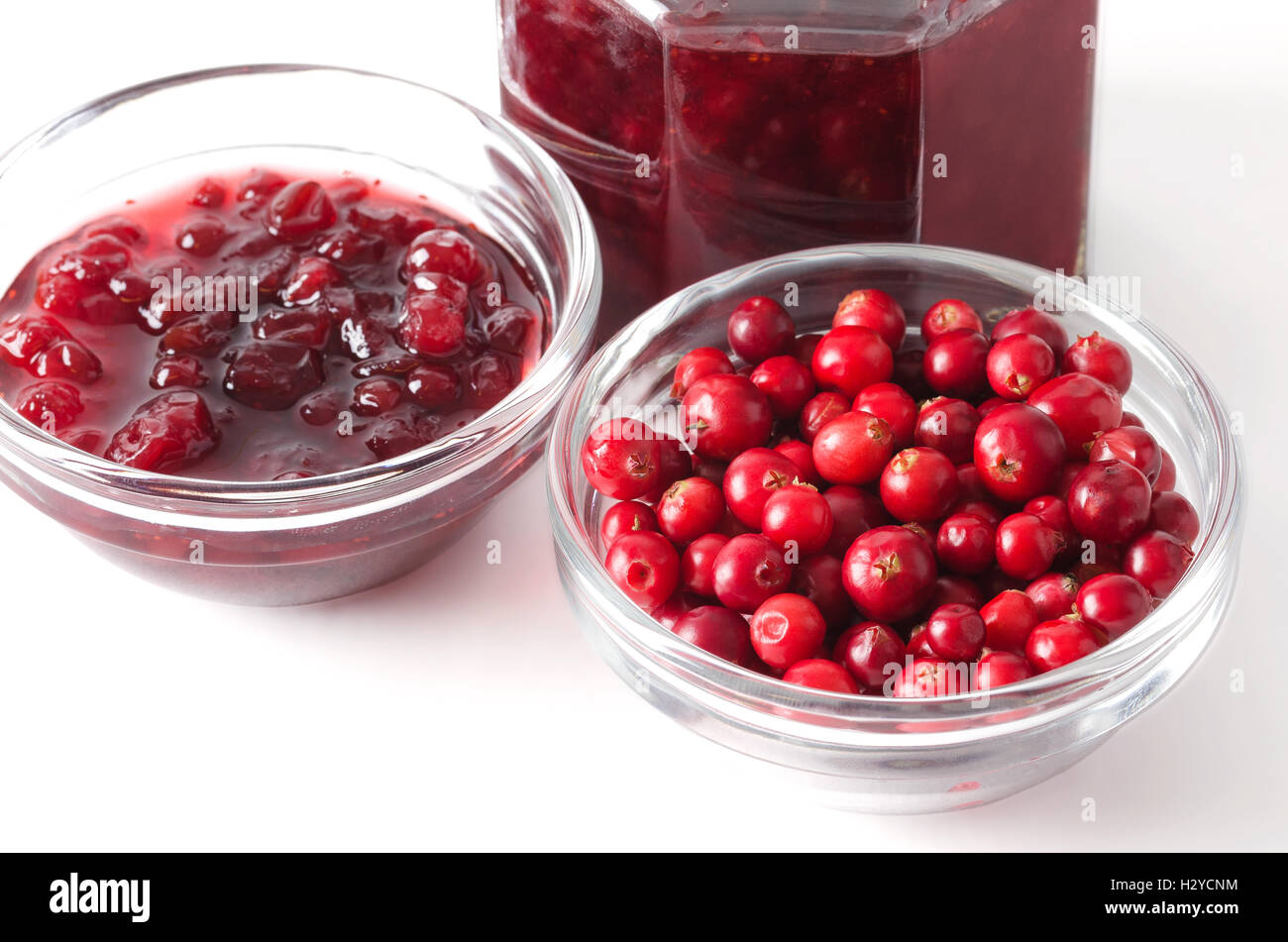 Lingonberries e lingonberry jam in ciotole in vetro su bianco. Rossi freschi Frutti del Vaccinium vitis-idaea, anche mirtillo rosso. Foto Stock