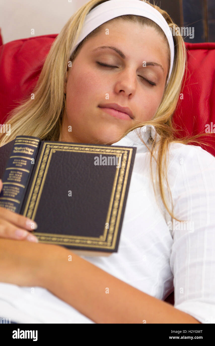 Giovane donna addormentati durante la lettura su un divano Foto Stock