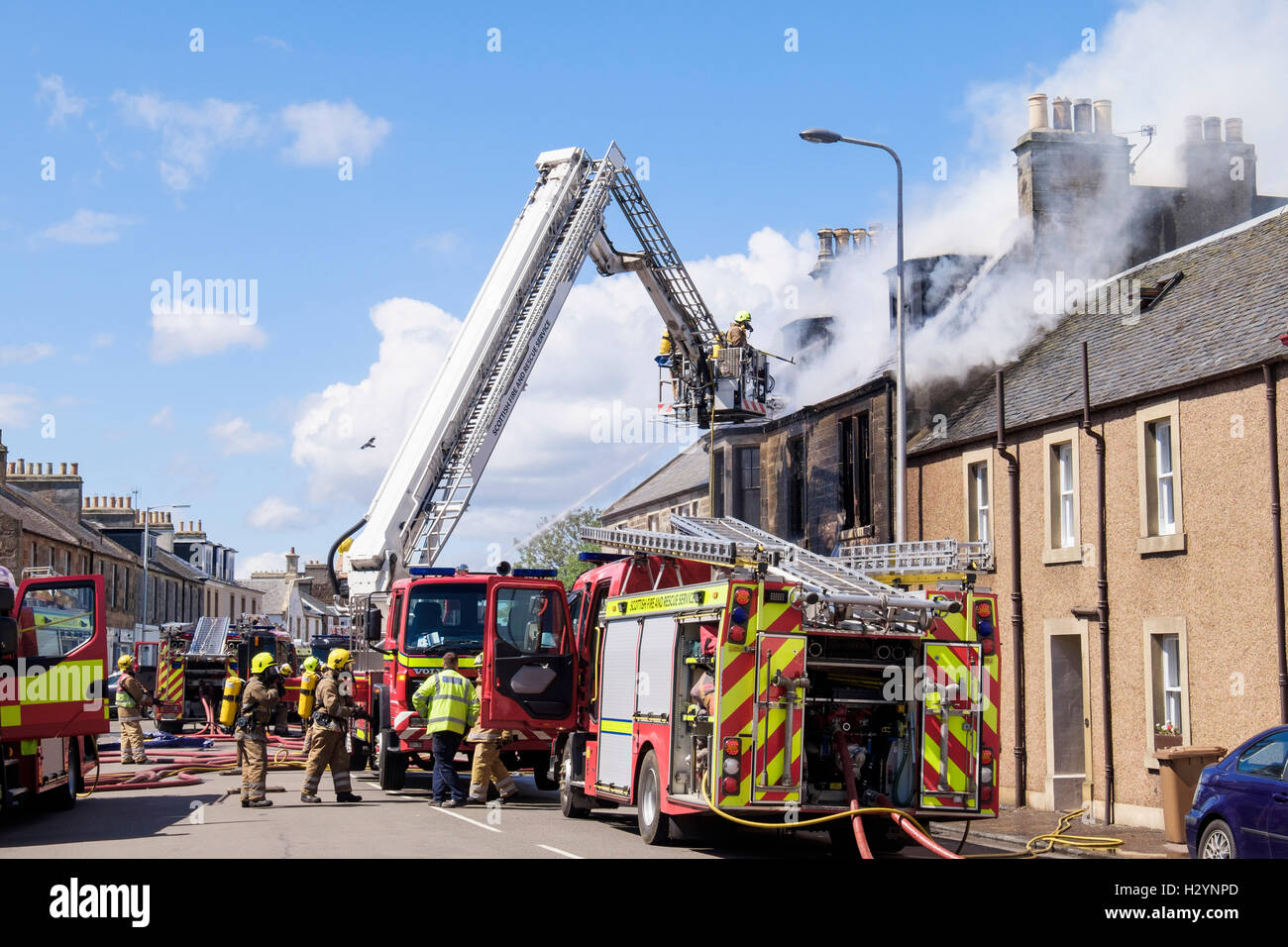 Scottish fuoco e il servizio di soccorso dei Vigili del fuoco su una scala che combatte contro un edificio in fiamme in Elie e Earlsferry, Fife, Scozia, Regno Unito Foto Stock