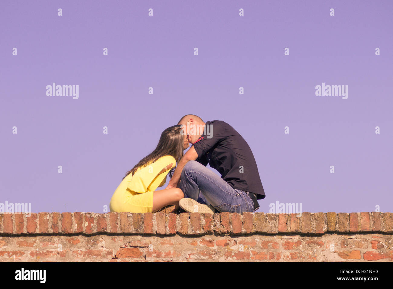 Coppia giovane 20s kissing seduta muro di mattoni Foto Stock