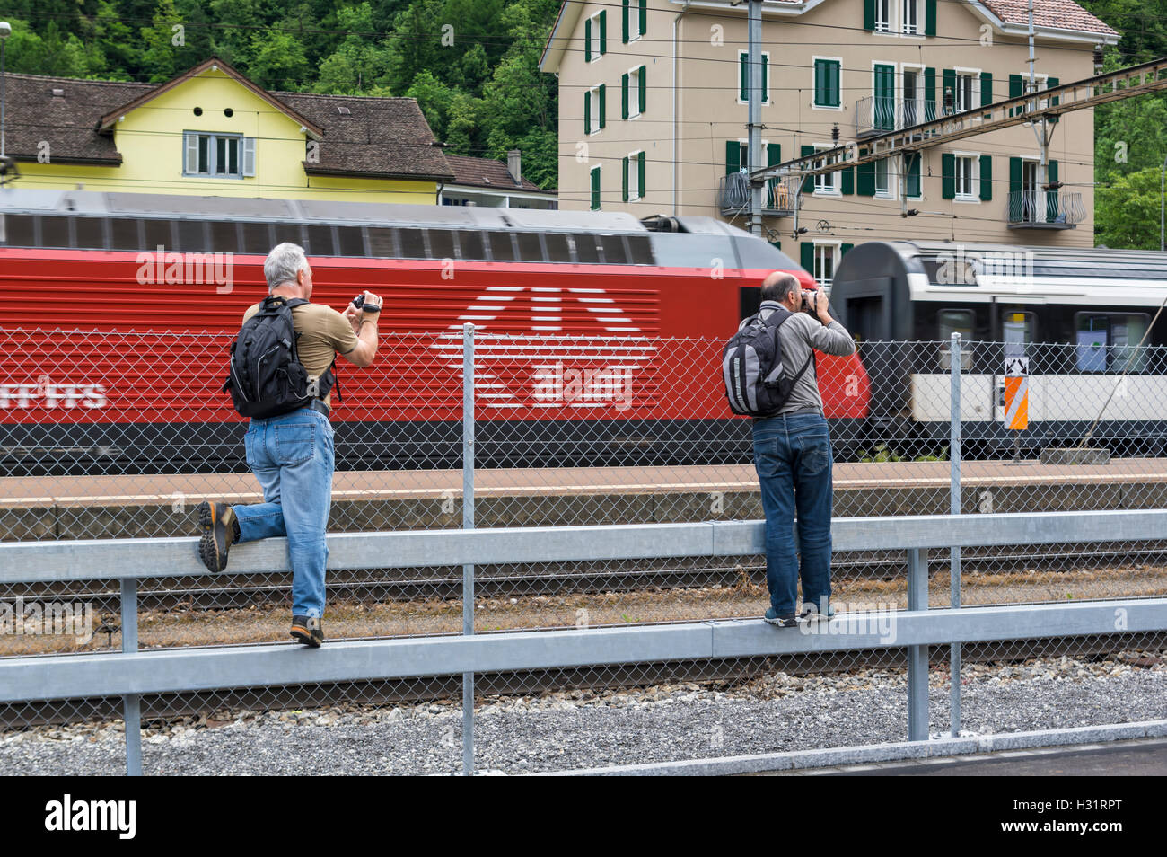 Trainspotters riprese video e le foto del passaggio di un treno con una locomotiva di colore rosso con le FFS Ferrovie Federali Svizzere logo. Erstfeld, Svizzera. Foto Stock