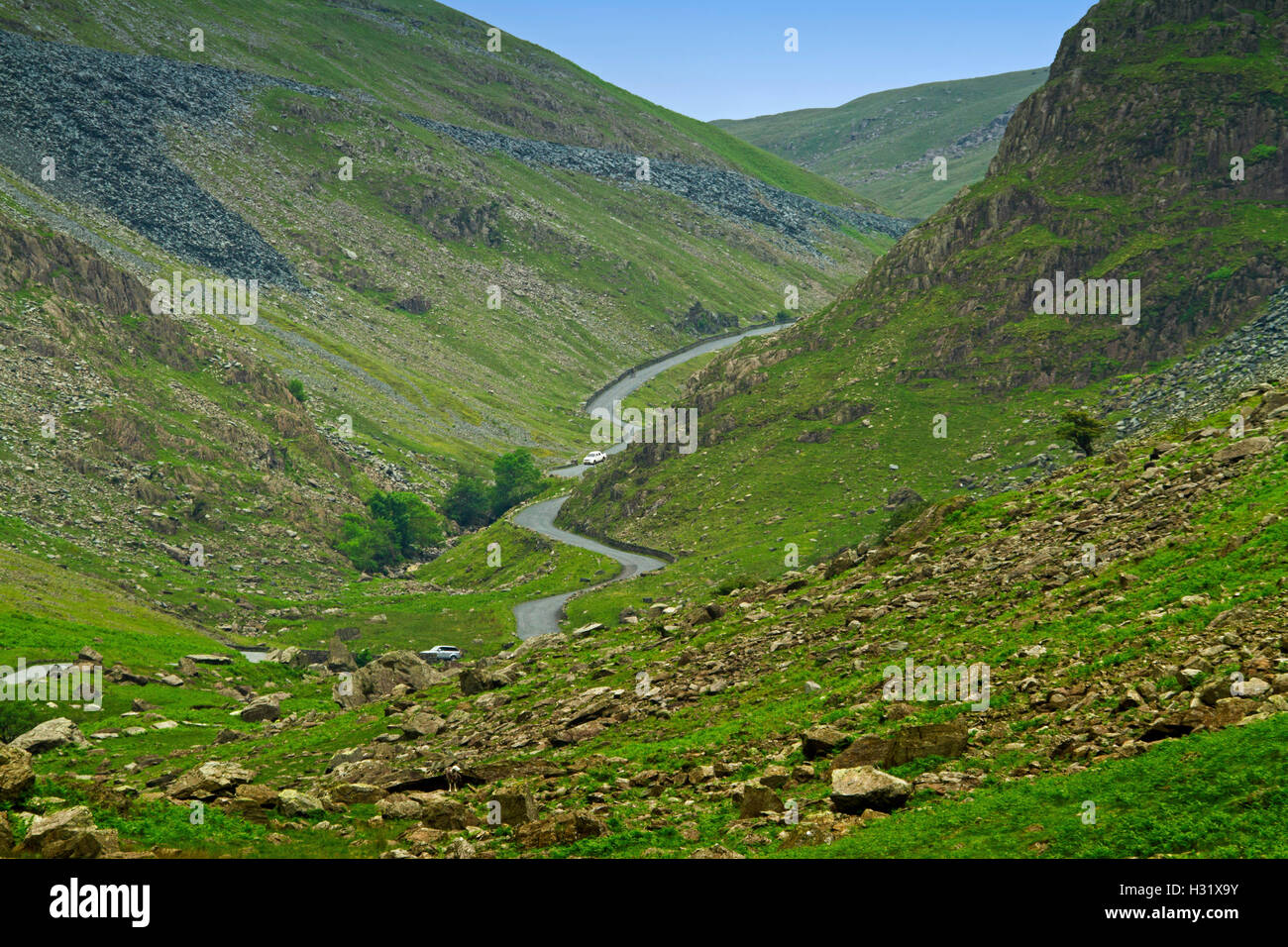 Strada stretta con auto serpeggiando attraverso la profonda valle tra sassoso brulla colline smeraldo a Honister Pass nel Lake District Cumbria, Inghilterra Foto Stock