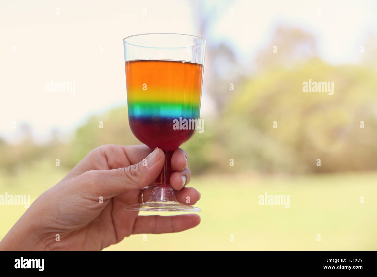Mano che tiene un bicchiere di rainbow jelly nel parco Foto Stock