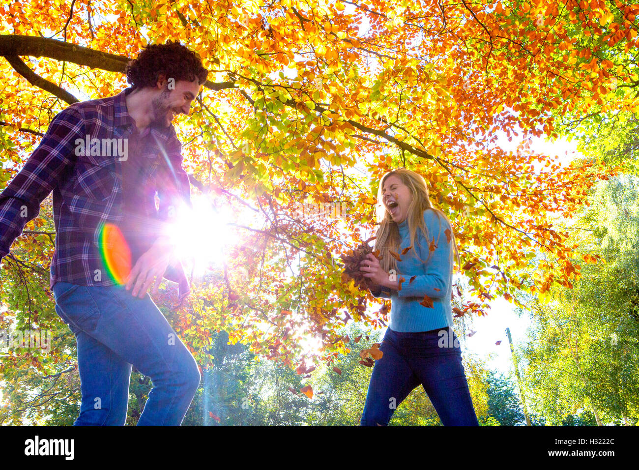 Coppia giovane divertendosi in autunno. Essi stanno gettando lascia ad ogni altra sotto gli alberi. Foto Stock