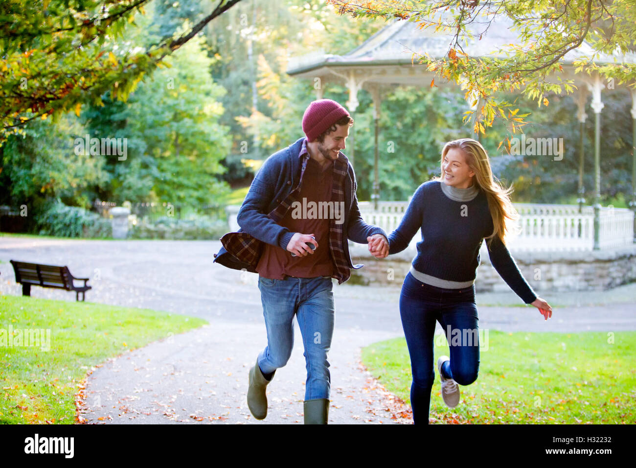 Coppia giovane correndo insieme attraverso un parco in autunno. Foto Stock