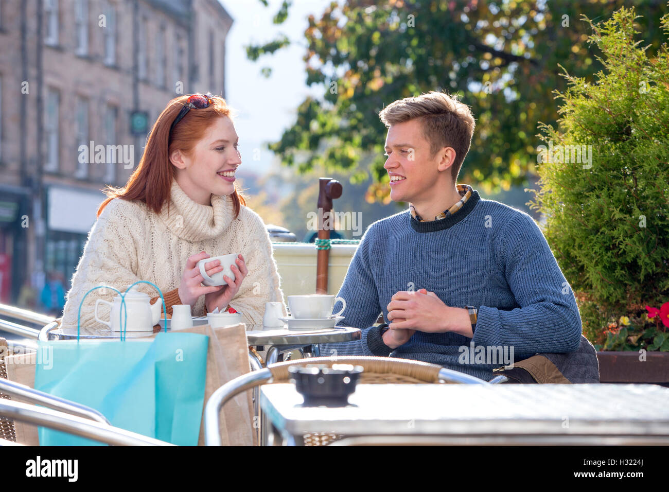 Coppia giovane gustando una tazza di tè in un cafe insieme. Essi sono seduti all'aperto nella città. Foto Stock