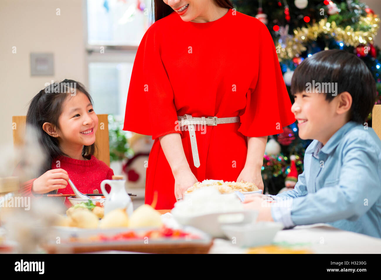 Famiglia cinese avente la cena di Natale. La madre è in piedi, imbutitura di cibo per tutti. I bambini sono a ridere insieme. Foto Stock