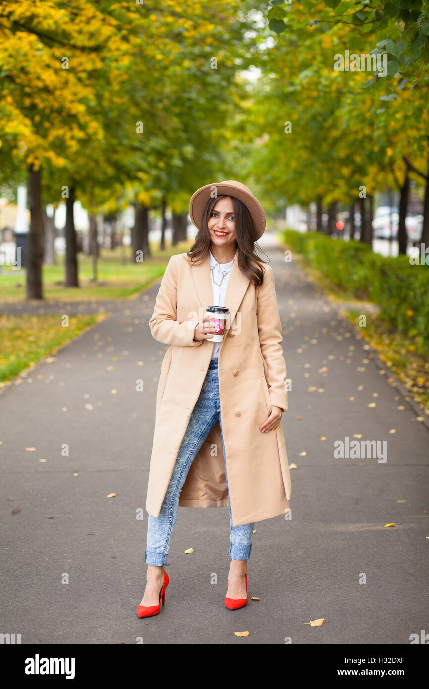 Ritratto di ragazza con caffè in red shoes coat, hat sullo sfondo di alberi di autunno Foto Stock