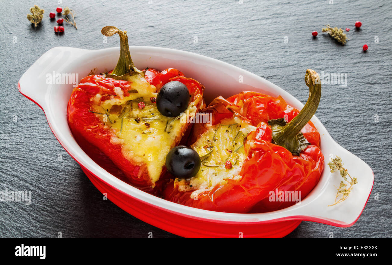 Rosso Farcite i peperoni con il formaggio feta e olive in rosso e bianco piatto di cottura su pietra nera dello sfondo. Foto Stock