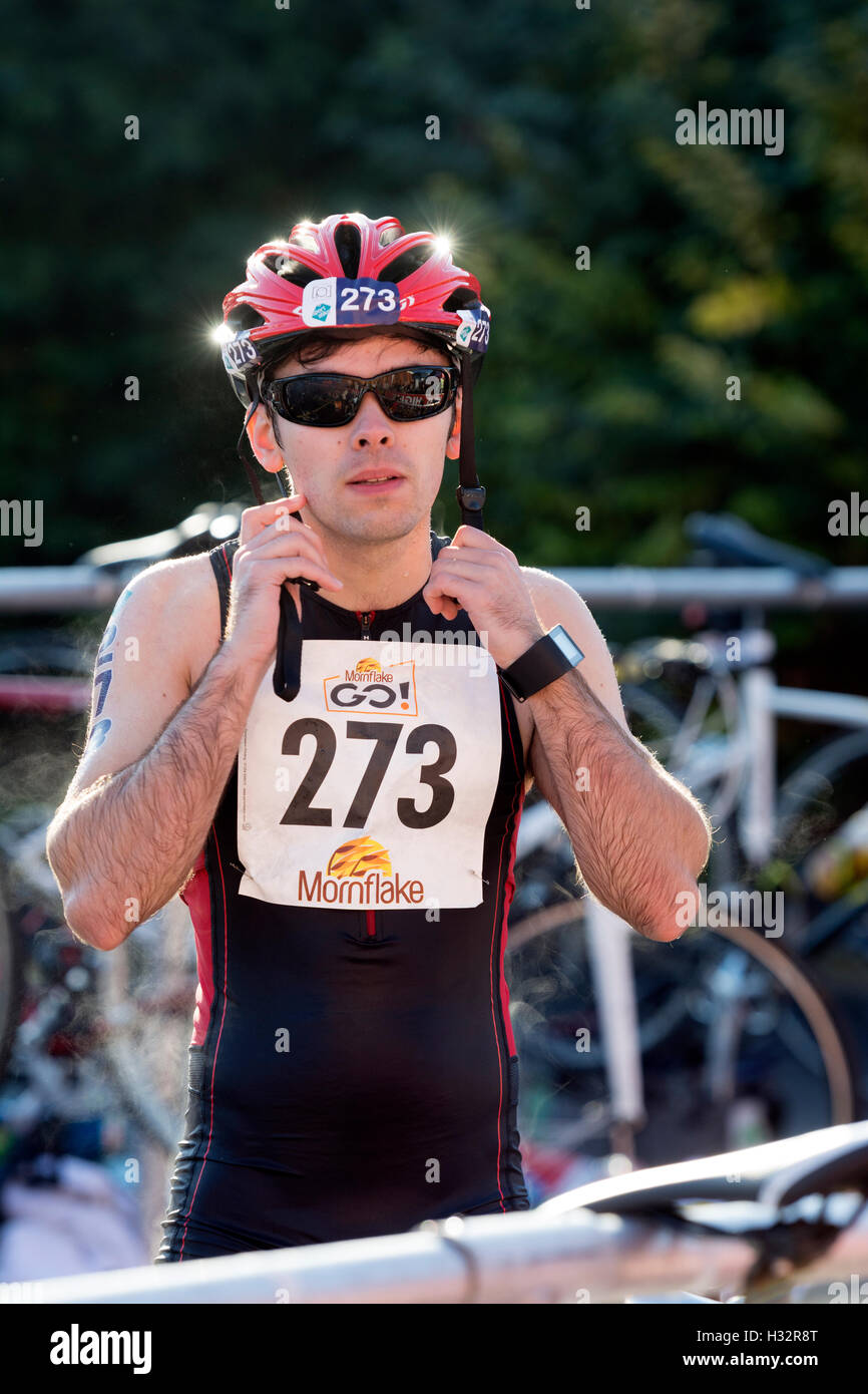 Concorrente maschile mettendo sul casco di ciclo nella zona di transizione, Warwickshire Triathlon, Stratford-upon-Avon, Regno Unito Foto Stock