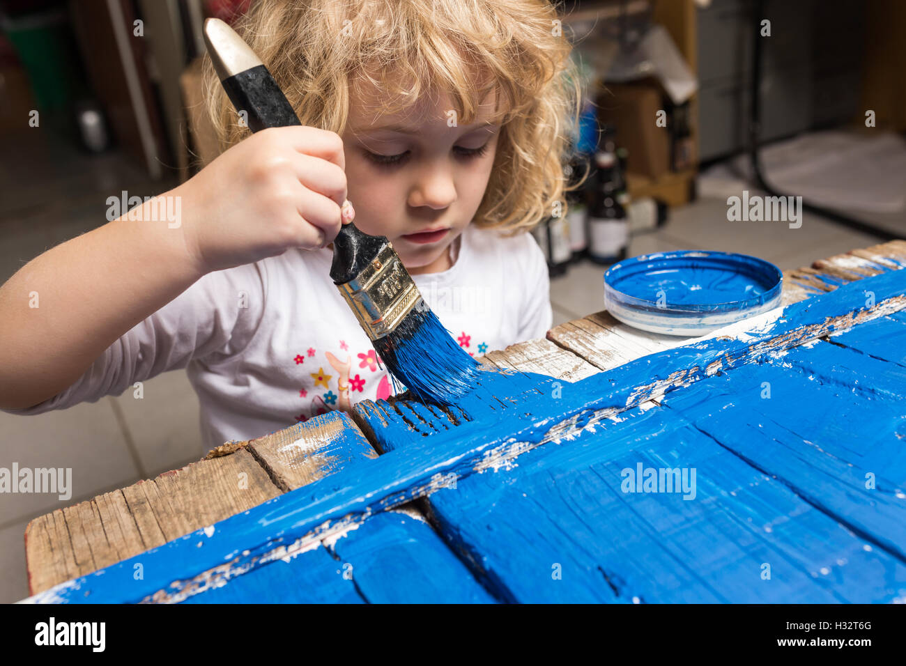 Bambina di verniciatura di un tavolo di legno con lo strumento Pennello, colore blu Foto Stock