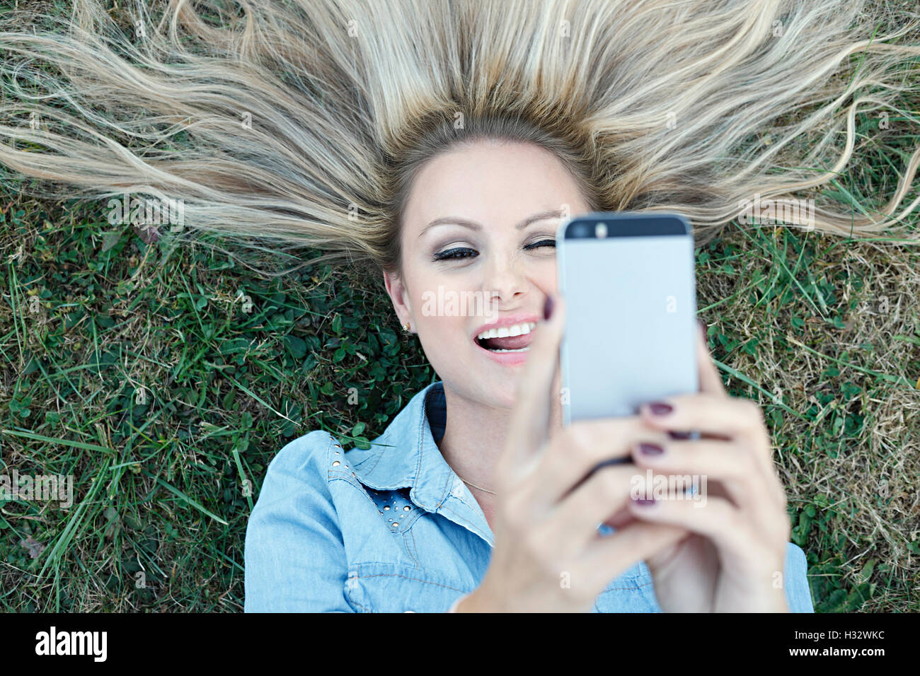 Giovane e bella bionda sdraiati sull'erba e tenendo selfie Foto Stock