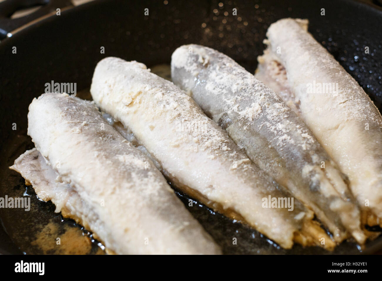 Nasello fritto di filetto di pesce in una padella in cucina Foto Stock