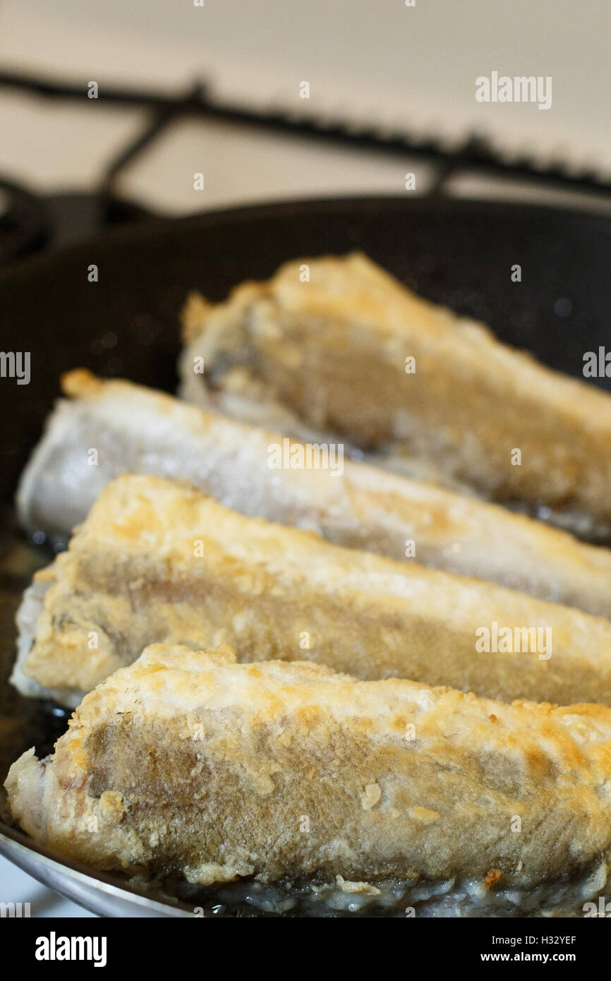 Nasello fritto di filetto di pesce in una padella in cucina Foto Stock