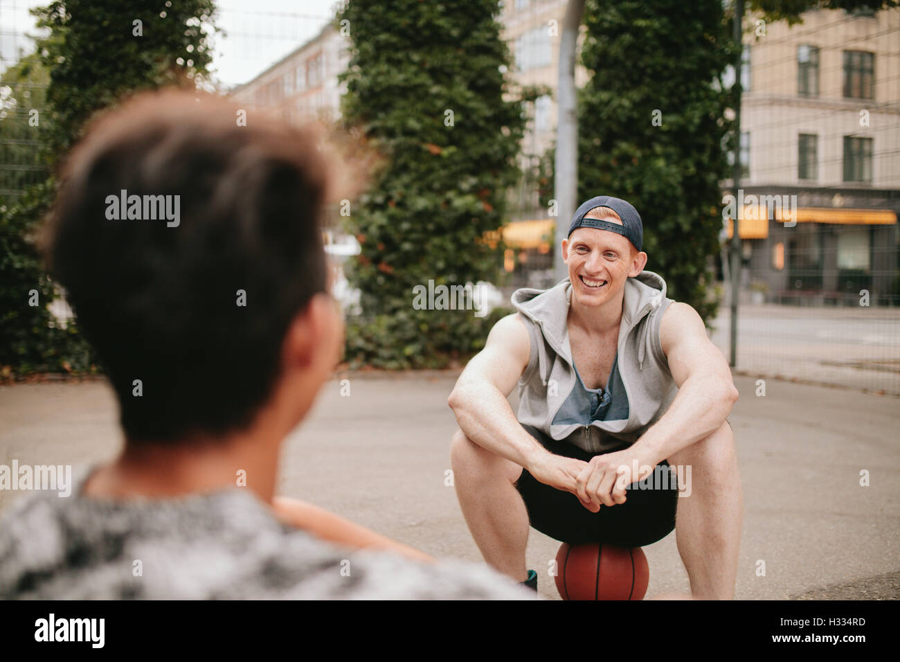 Sorridente giovane ragazzo seduto su un campo da basket e parlando con un amico. Due amici rilassante dopo giocare a basket sulla corte. Foto Stock