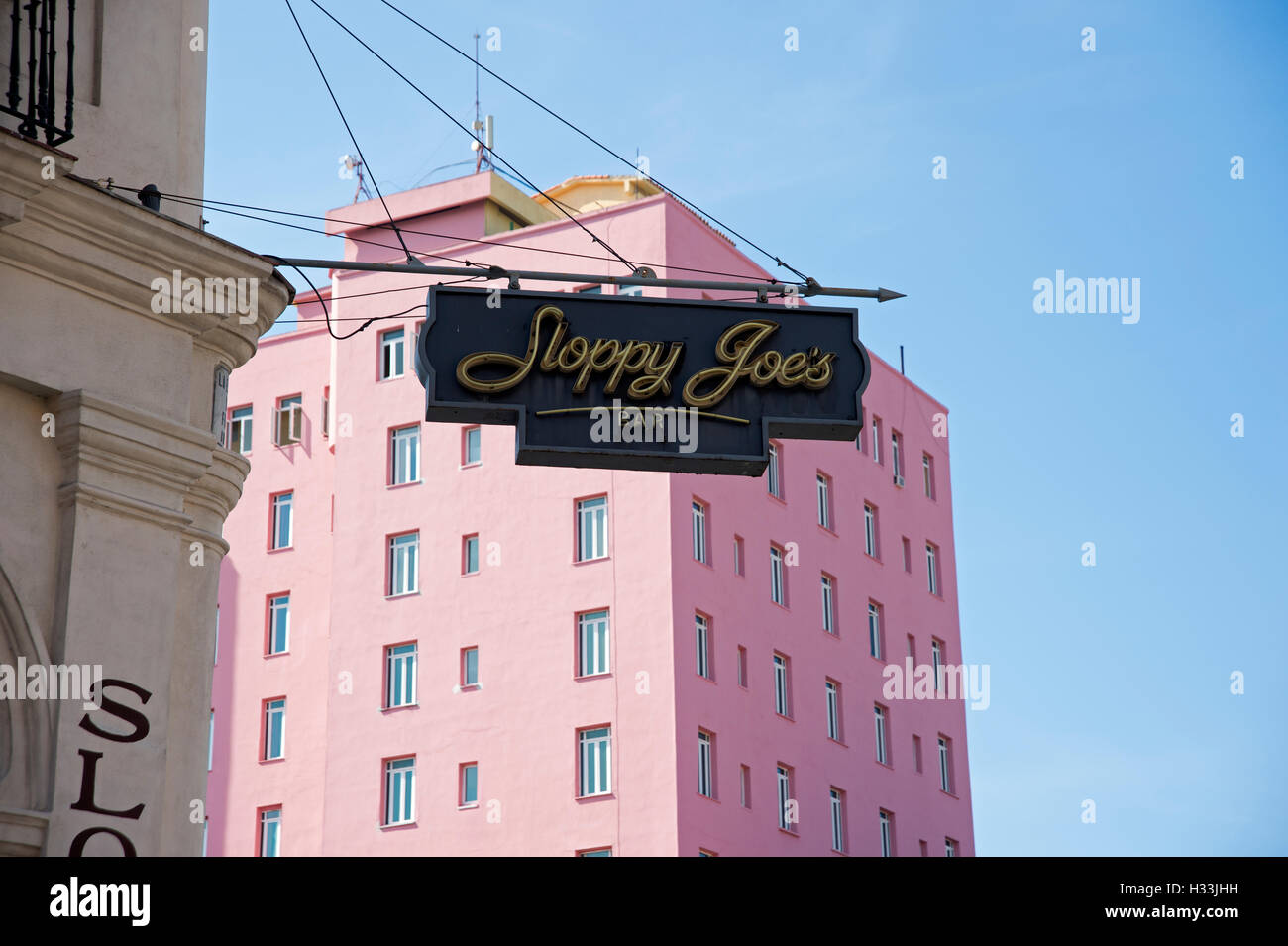 Il segno per sciatta Joe's bar di Havana sporgente dalla barra con un dipinto di rosa edificio art-deco in background Foto Stock