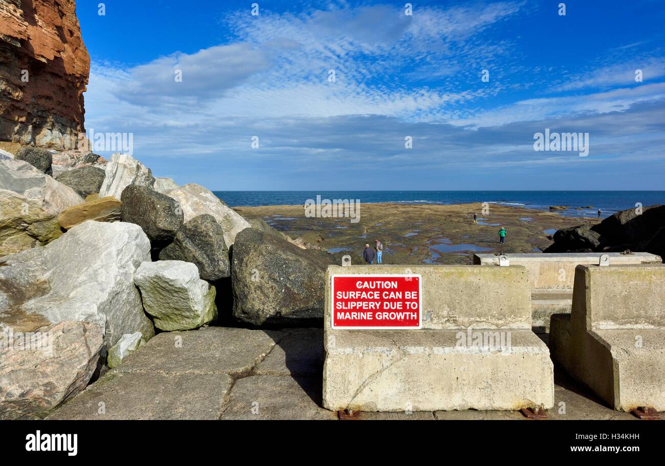 Il simbolo di attenzione superficie può essere scivoloso a causa di crescita marine. Staithes North Yorkshire England Regno Unito Foto Stock