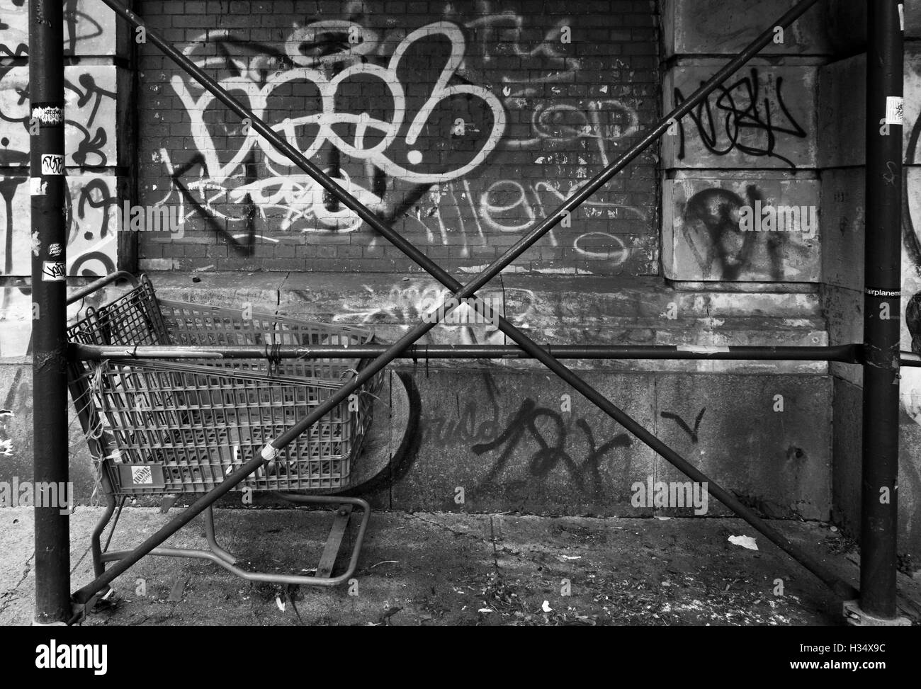 Monocromatico immagine granulosa di ponteggi attraversato i poli con abbandonato carrello della spesa e una coperta di graffiti parete in New York Foto Stock