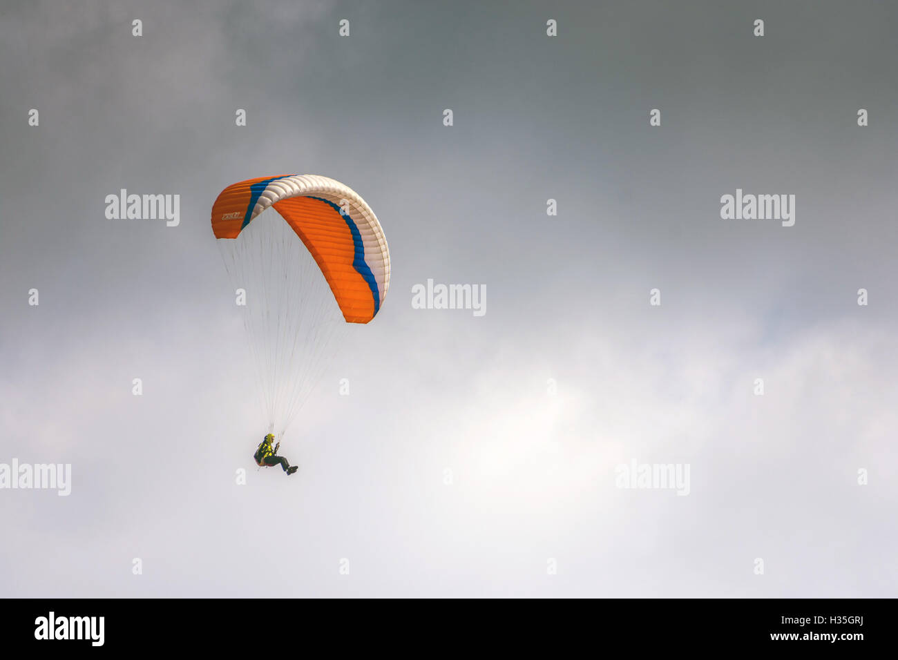 Da solista parapent arancione, parapendio, hanglider battenti, contro il grigio cielo grigio Foto Stock