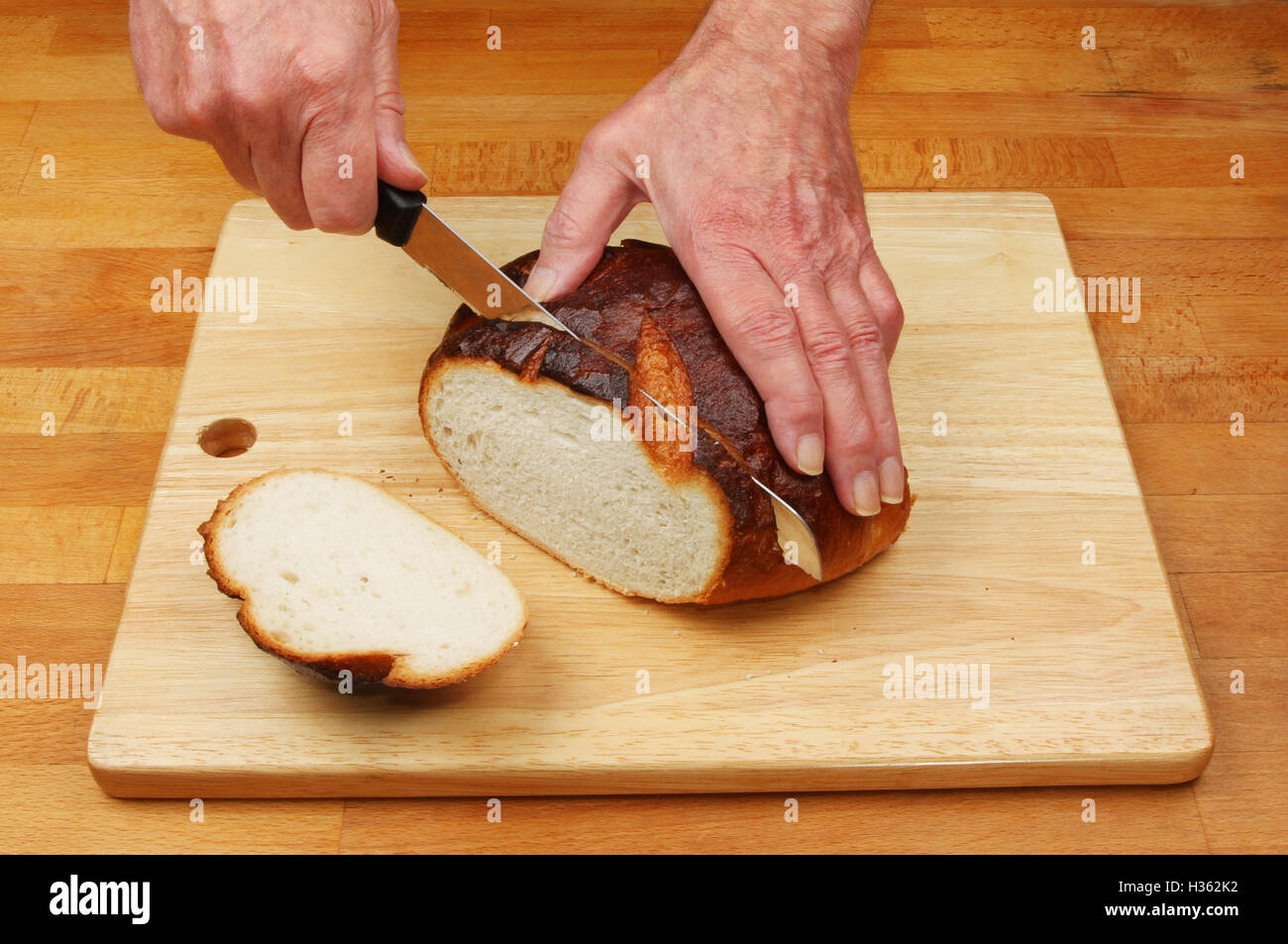 Le mani un taglio ben cotto il pane rustico focaccia su un piano di lavoro di una cucina Foto Stock