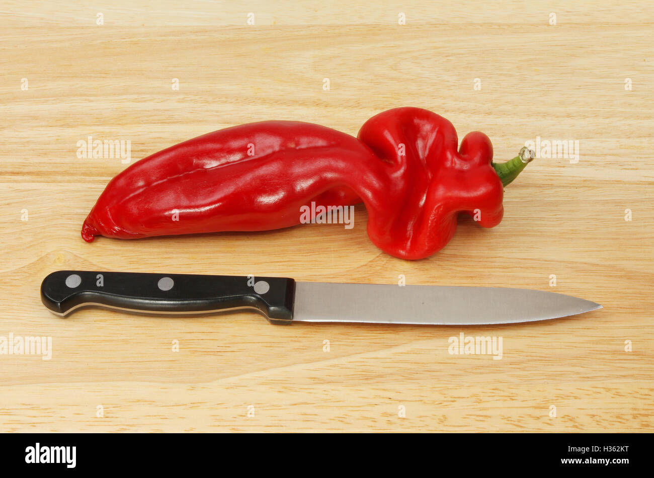 Sottolineato peperone rosso e il coltello da cucina su un tagliere di legno Foto Stock