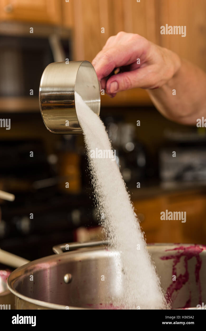 Versare lo zucchero in una pentola per la cottura o per la cottura di vivande. Foto Stock