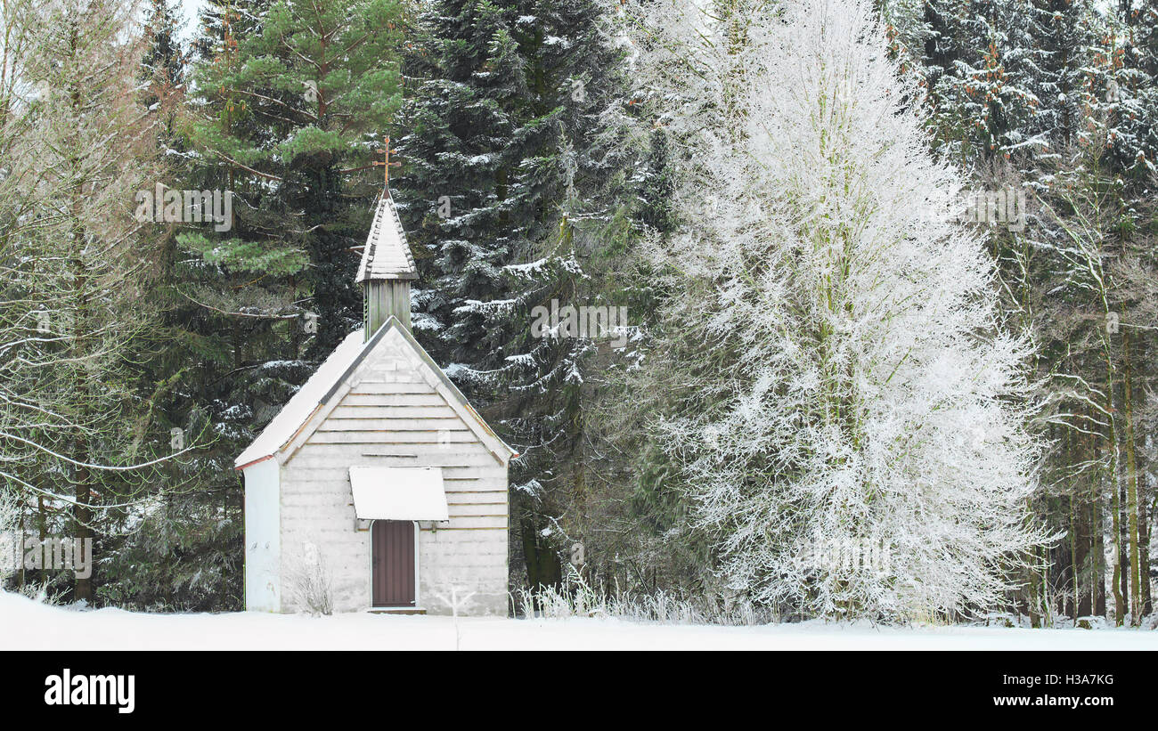 Tranquilla vista invernale di poco snow-capped rurale chiesa in legno su snowfield radura nel bosco surgelati Foto Stock