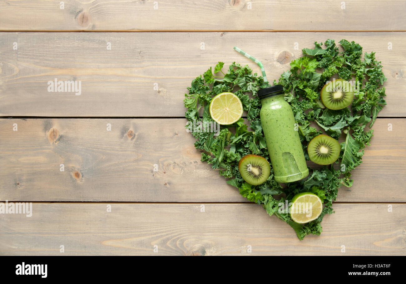 Verde bottiglia smoothie con ingredienti in una forma di cuore al di sopra di un tavolo di legno Foto Stock