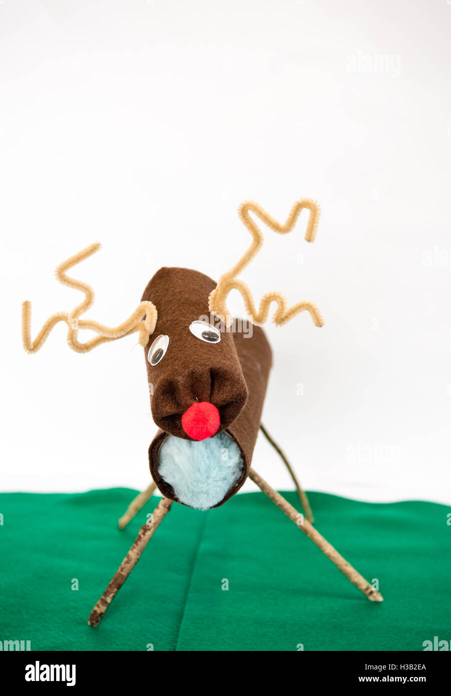Un divertente wonky artigianale di Rudolph la renna natale decorazione realizzata dal riciclaggio di rotoli di carta igienica e pulitori della tubazione su un po' di feltro verde Foto Stock