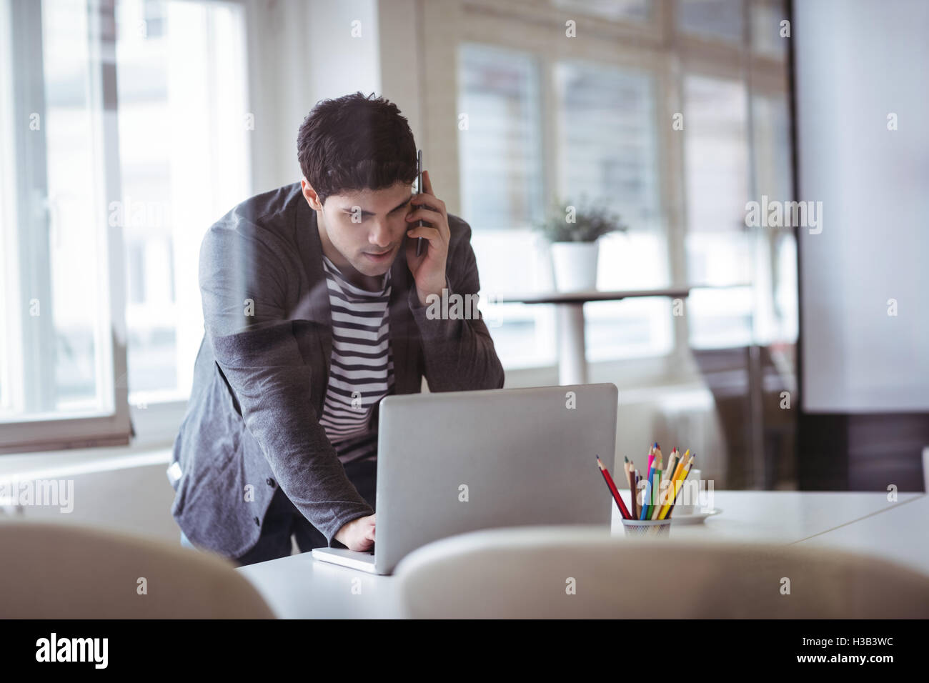 Editor foto parlando al telefono cellulare mentre si lavora laptop Foto Stock