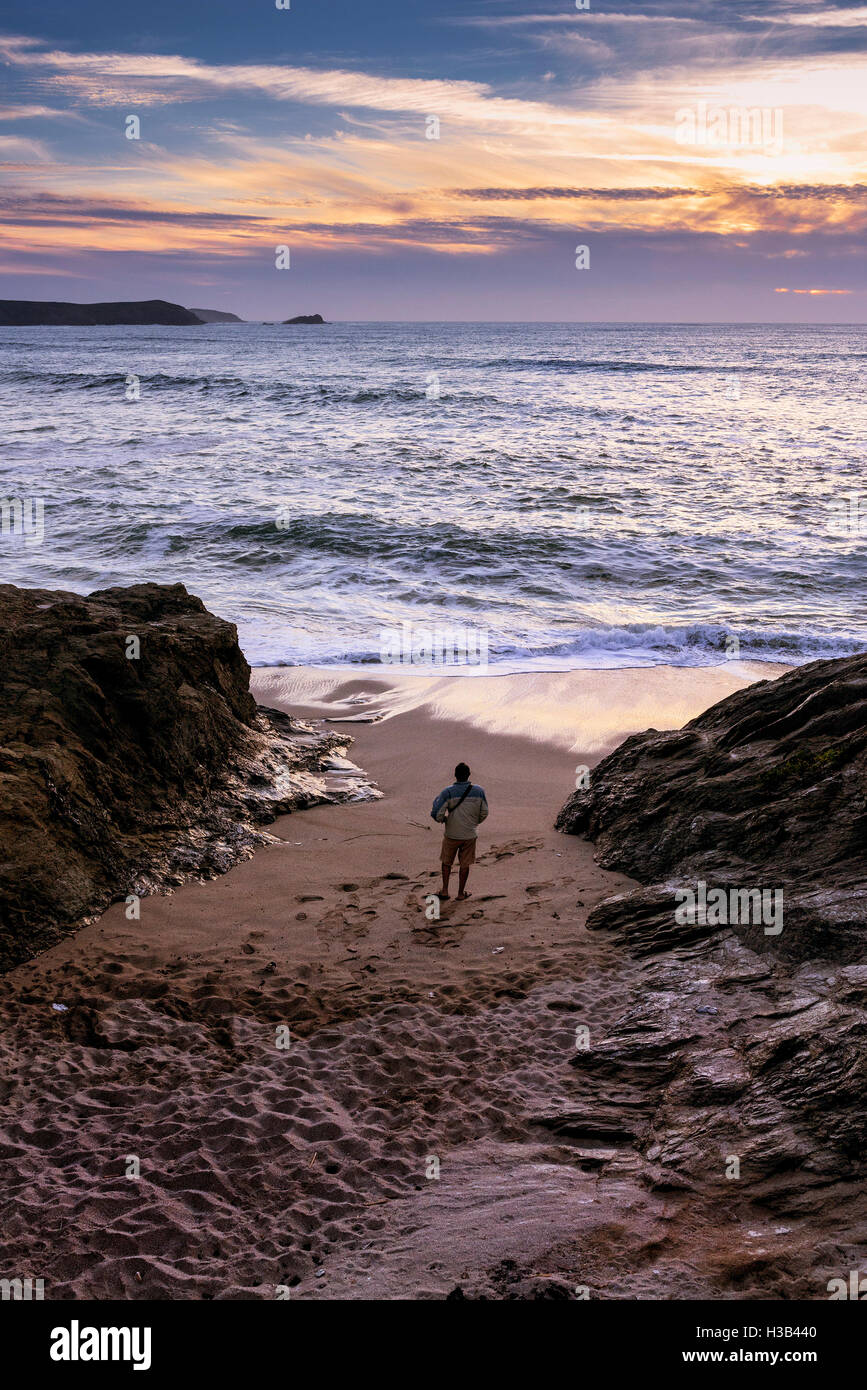 Un uomo si trova sulla spiaggia a poco Fistral come il sole tramonta. Foto Stock
