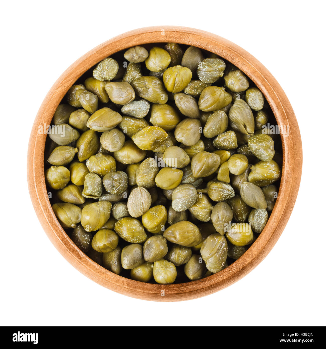 Capperi in ciotola di legno su sfondo bianco. Prodotti commestibili boccioli di fiori di Capparis spinosa, cappero bush o Flinders rose. Foto Stock