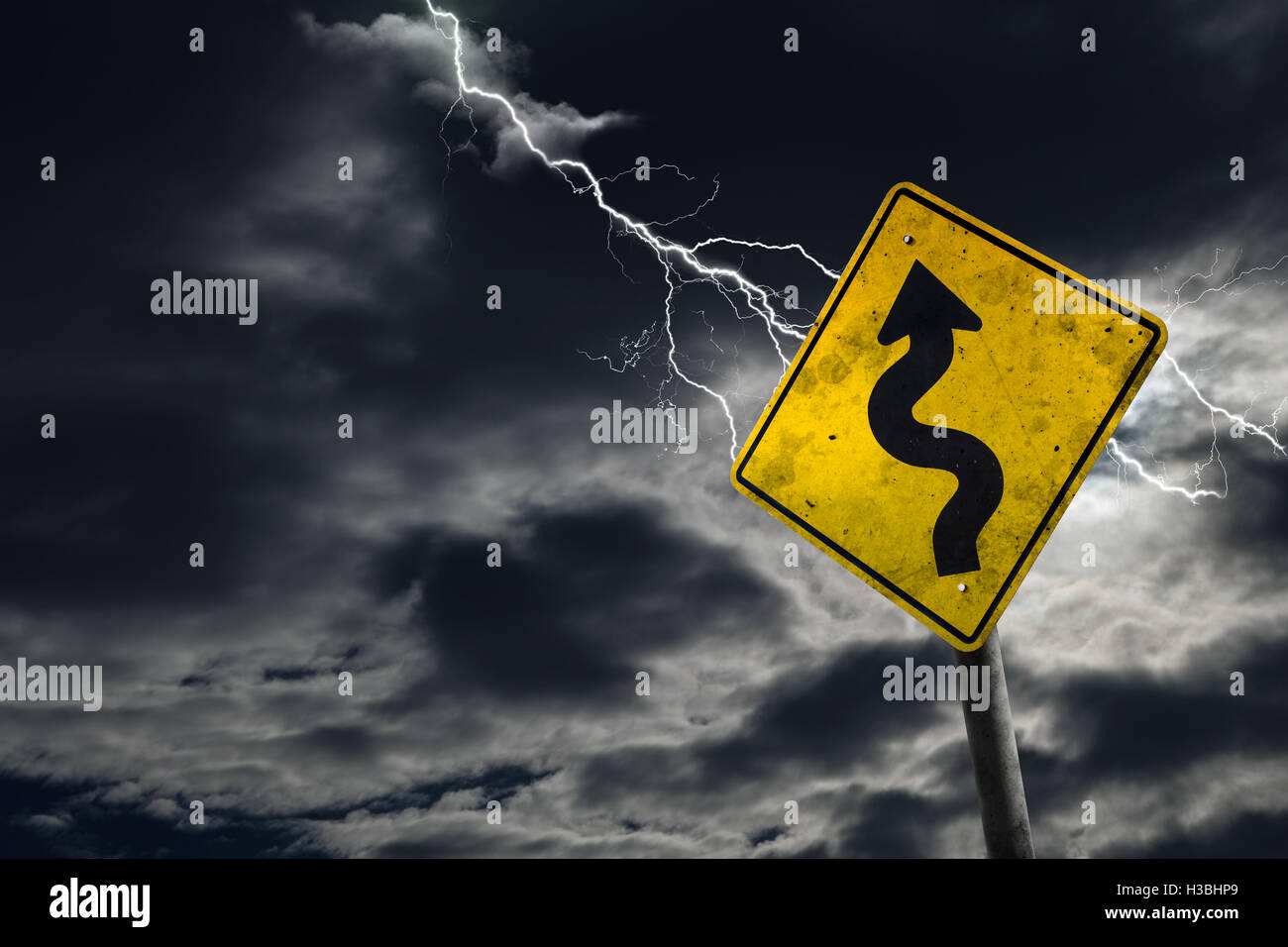 Winding Road Sign contro un sfondo tempestoso con lampi e copia di spazio. Sporco e cartello angolato aggiunge al dramma. Foto Stock