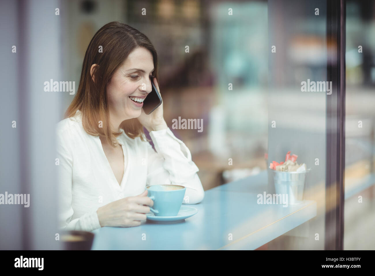 Donna che mantiene tazza di caffè e parlando al telefono cellulare Foto Stock